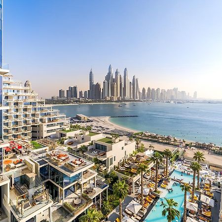 Five Palm Jumeirah Dubai Esterno foto The photo depicts a stunning seaside view featuring modern architectural structures. In the foreground, there are luxurious buildings and a pool area surrounded by palm trees. In the background, you can see a skyline of tall, contemporary skyscrapers